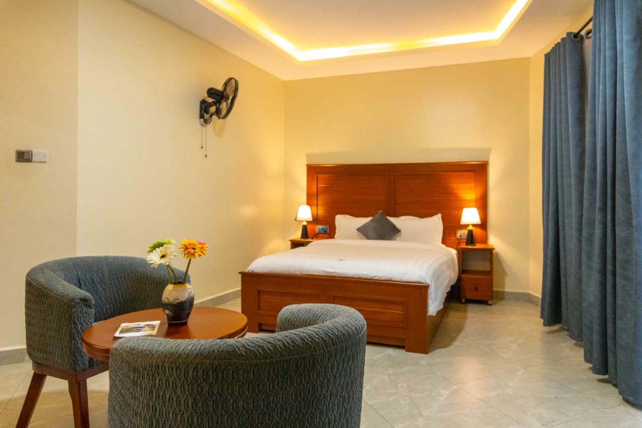 A cottage bedroom with armchairs by the bed under a warm lit ceiling