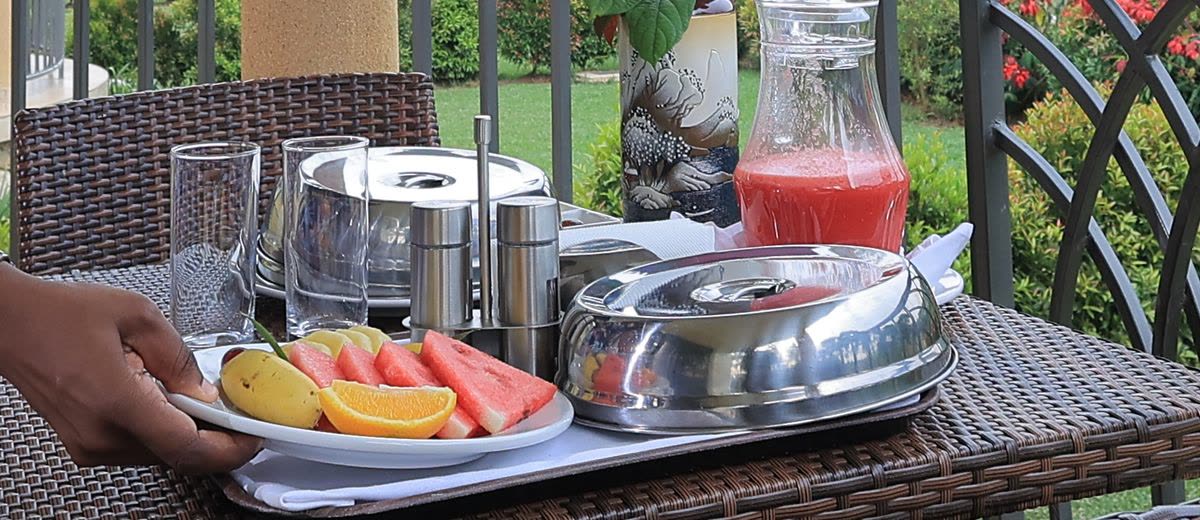 A breakfast tray with a fruit plate and covered dishes on a terrace table