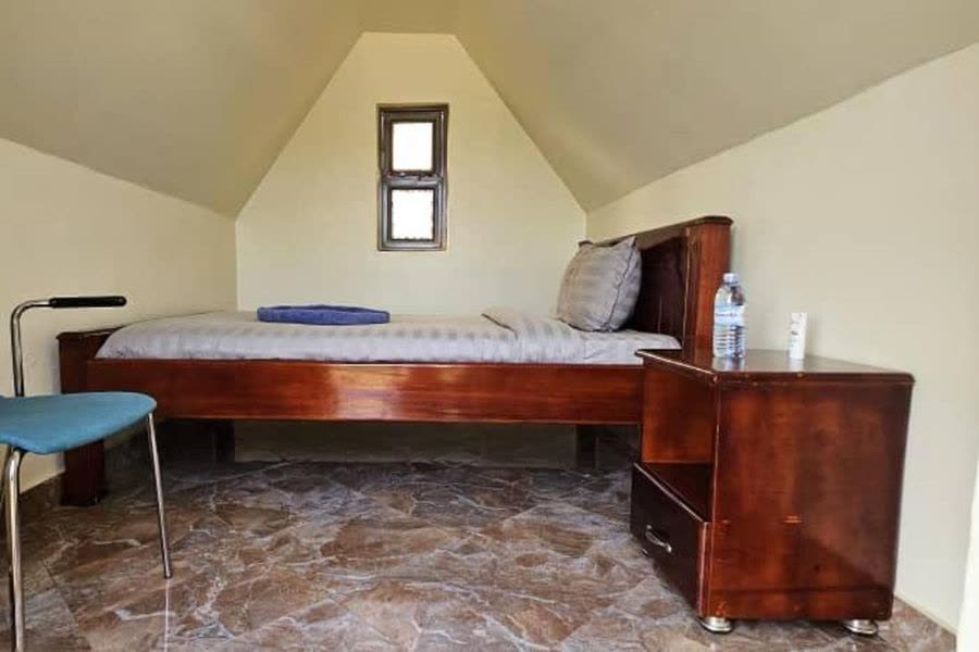 Inside an A-frame studio: a single bed, bedside cabinet and chair
