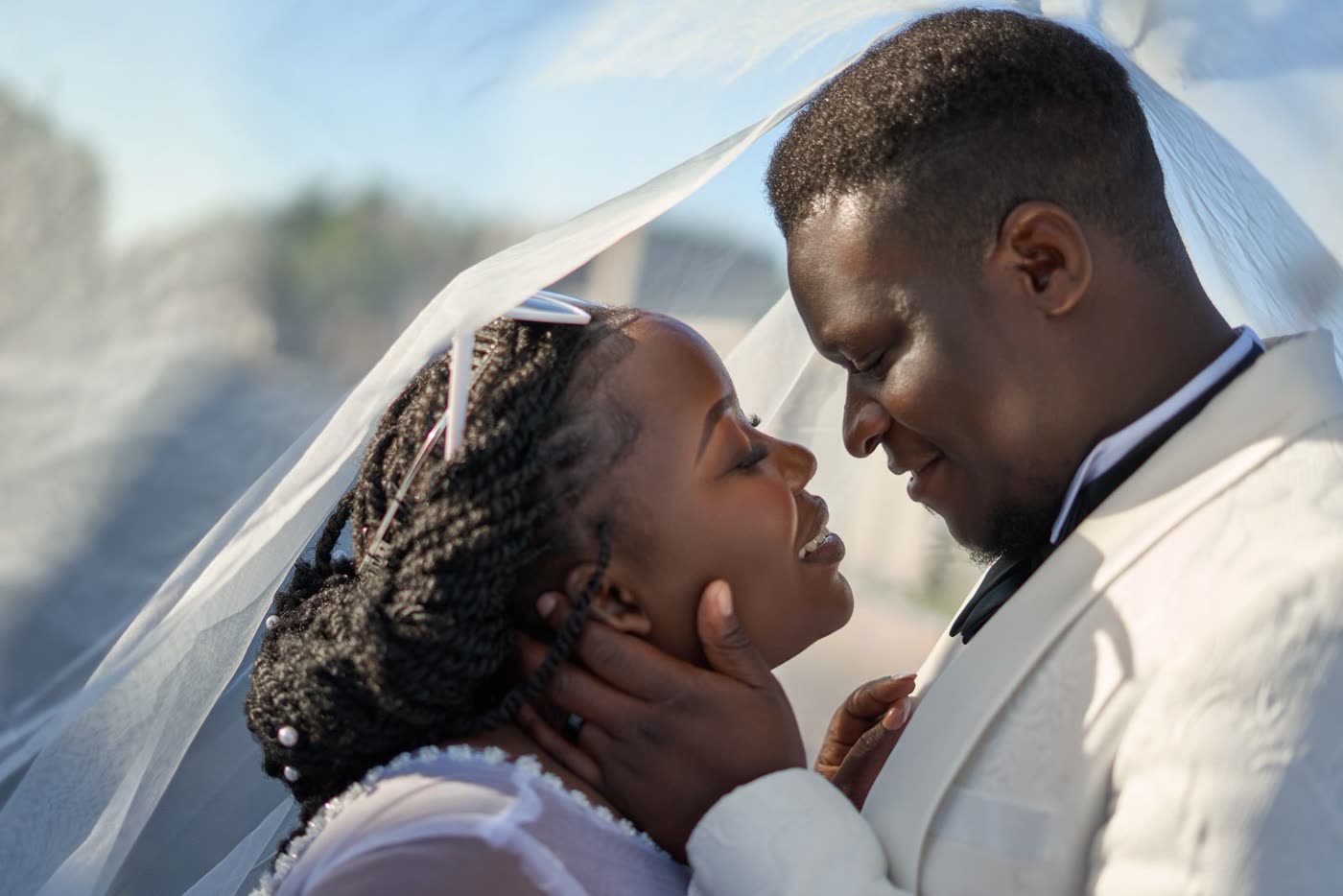 A couple sharing a tender moment under a veil in the sunlight