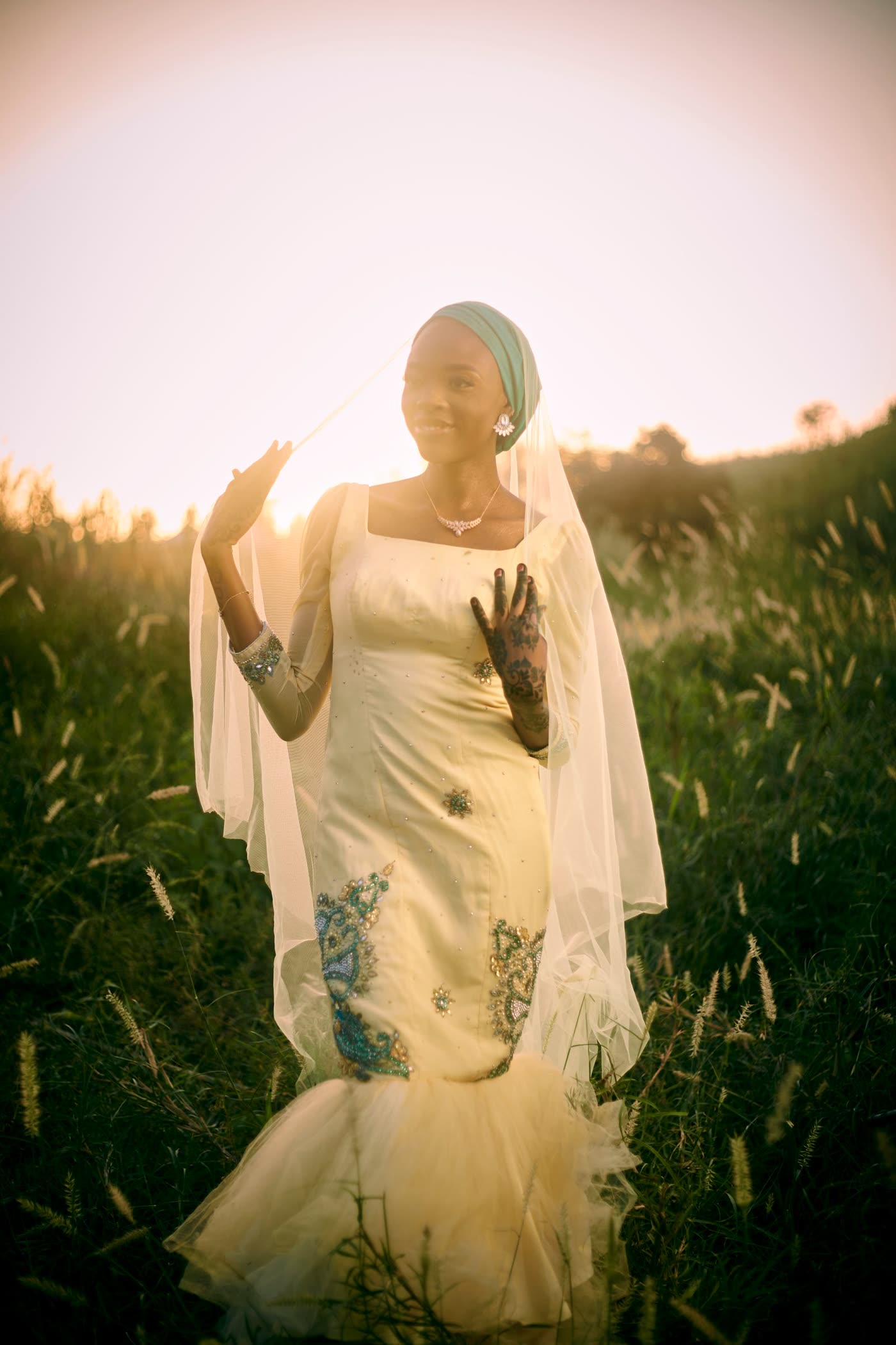A bride in a veil standing in tall grass at sunset